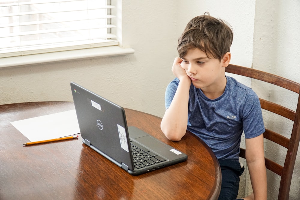 갈색 나무 테이블에 MacBook Pro를 사용하는 파란색 크루 넥 티셔츠를 입은 소년