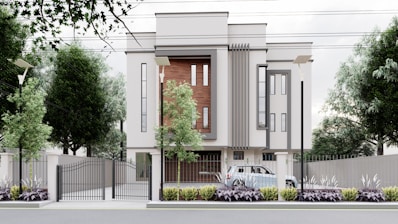 A modern, multi-story building with a minimalist design features large vertical windows and accent walls with wooden panels. The property is surrounded by a metal fence with a gate, and there are street lamps and tall trees along the perimeter. A car is parked inside the gated area, and the landscaped front garden is adorned with shrubs and plants.