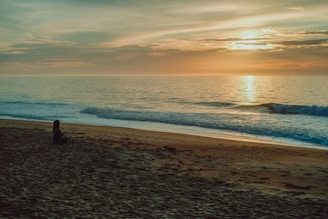 Woman sitting on a beach at sunset, looking out at the water in a quiet, reflective moment