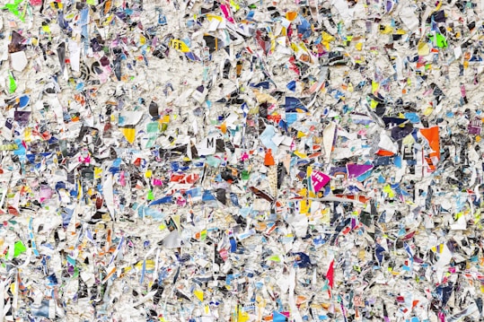 A chaotic and colorful mixture of torn paper pieces with various text, images, and colors scattered densely throughout. The image is a collage that creates a textured and vibrant appearance, making it difficult to focus on any single piece. The torn papers overlap and intersect, offering a visual representation of randomness and disorder.