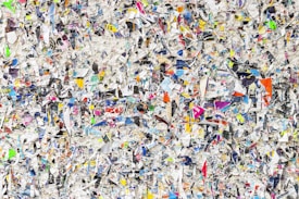 A chaotic and colorful mixture of torn paper pieces with various text, images, and colors scattered densely throughout. The image is a collage that creates a textured and vibrant appearance, making it difficult to focus on any single piece. The torn papers overlap and intersect, offering a visual representation of randomness and disorder.