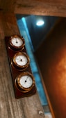 Three circular gauges mounted on a wooden panel are attached to a textured wall. The setting has industrial elements, with visible concrete surfaces and a soft ambient light that adds warmth to the scene.