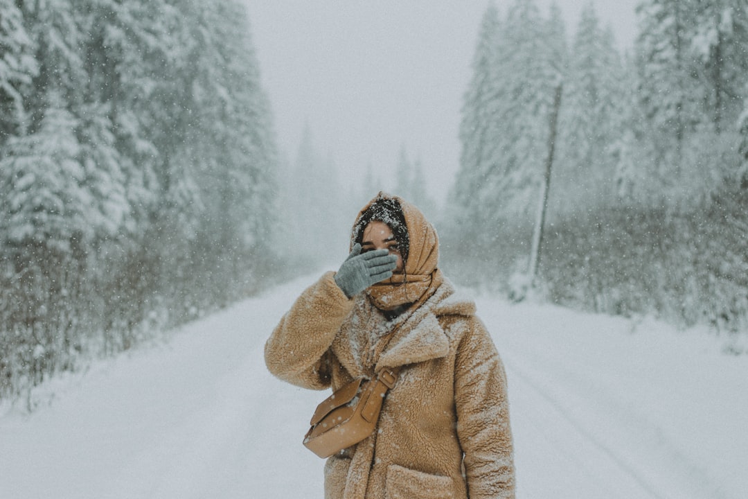 woman in brown coat standing on snow covered ground during daytime