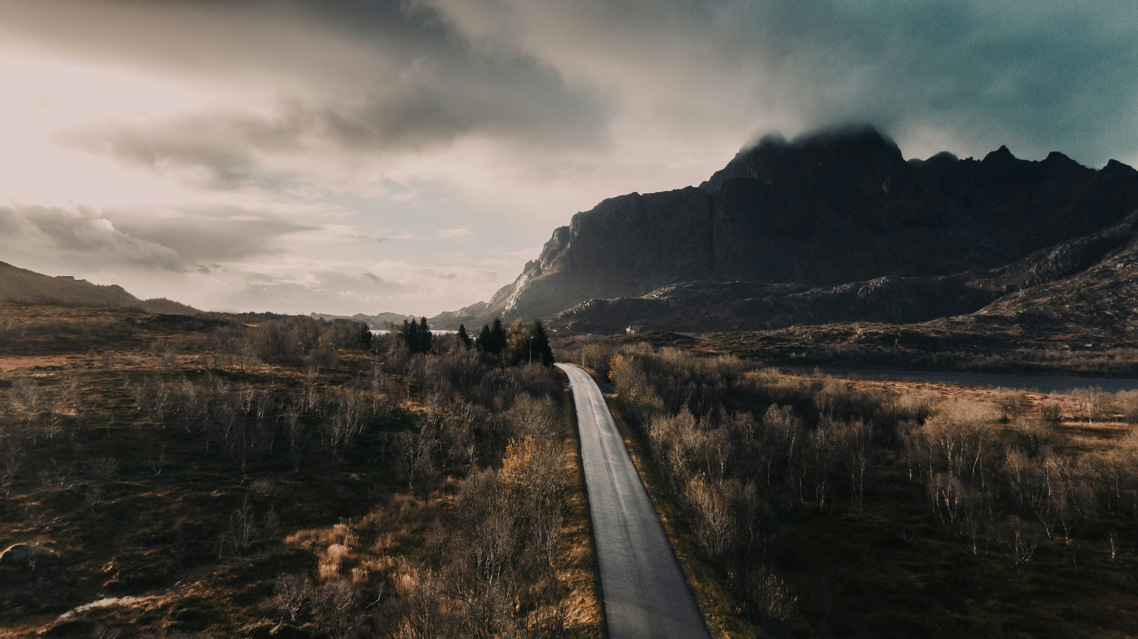 camino de concreto gris entre el campo de hierba marrón cerca de la montaña bajo nubes blancas durante el día