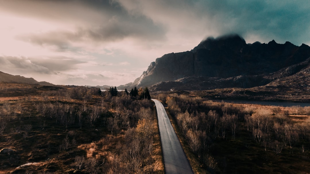 gray concrete road between brown grass field near mountain under white clouds during daytime