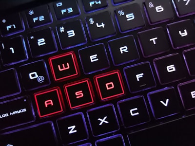 The image displays a close-up view of a keyboard with backlit keys. Most of the keys are illuminated in white, while the keys W, A, S, and D are highlighted in red, drawing attention to them. The arrangement suggests a focus on gaming-related keyboard use, as these keys are often used in games for navigation.