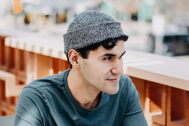 A man seated at a café patio, wearing a soft gray sweater and light denim jeans.
