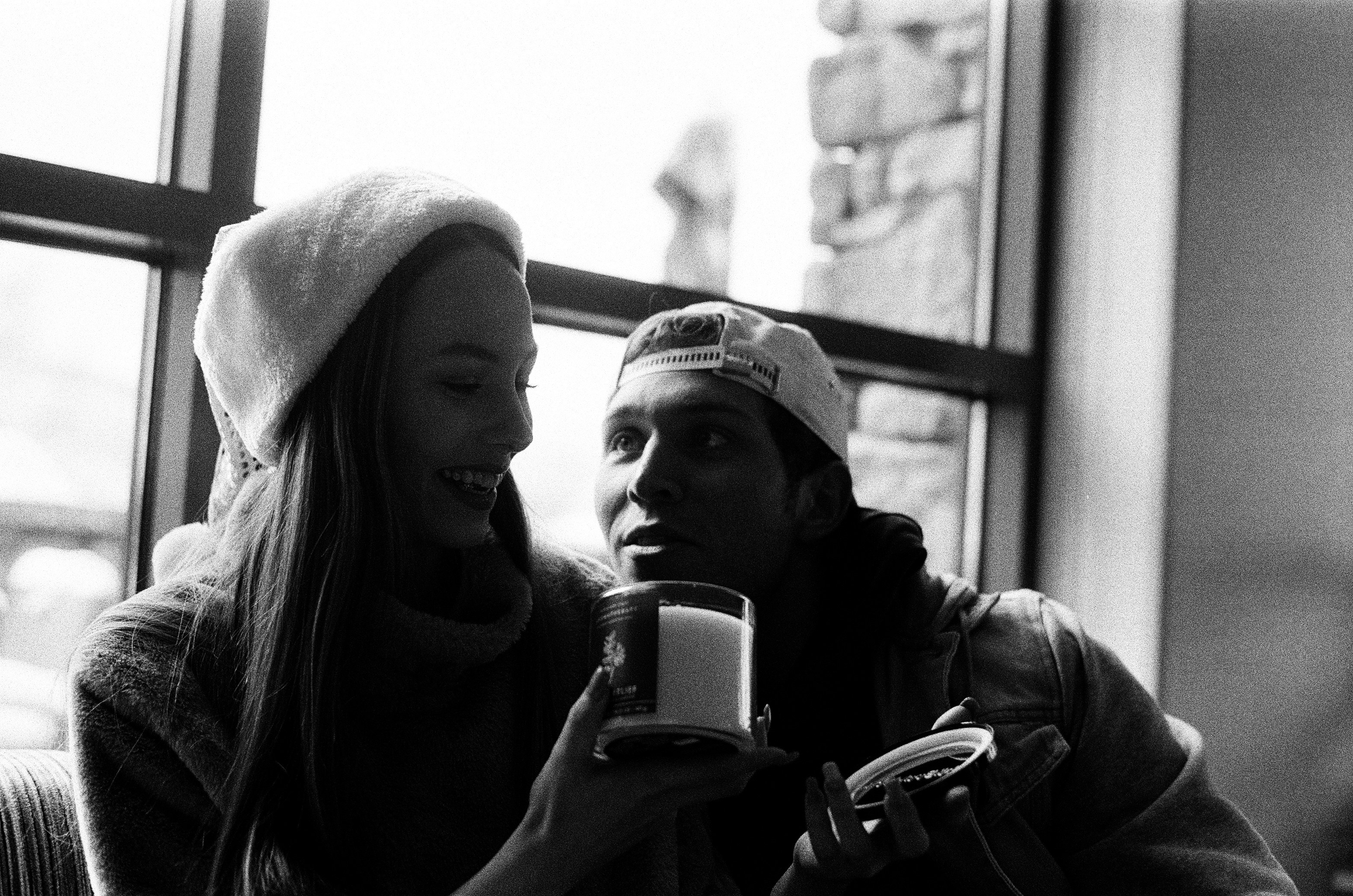 A young couple sitting together on a couch, looking surprised and laughing during an animated and revealing conversation.