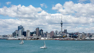 white sailboat on sea near city buildings under white clouds and blue sky during daytime