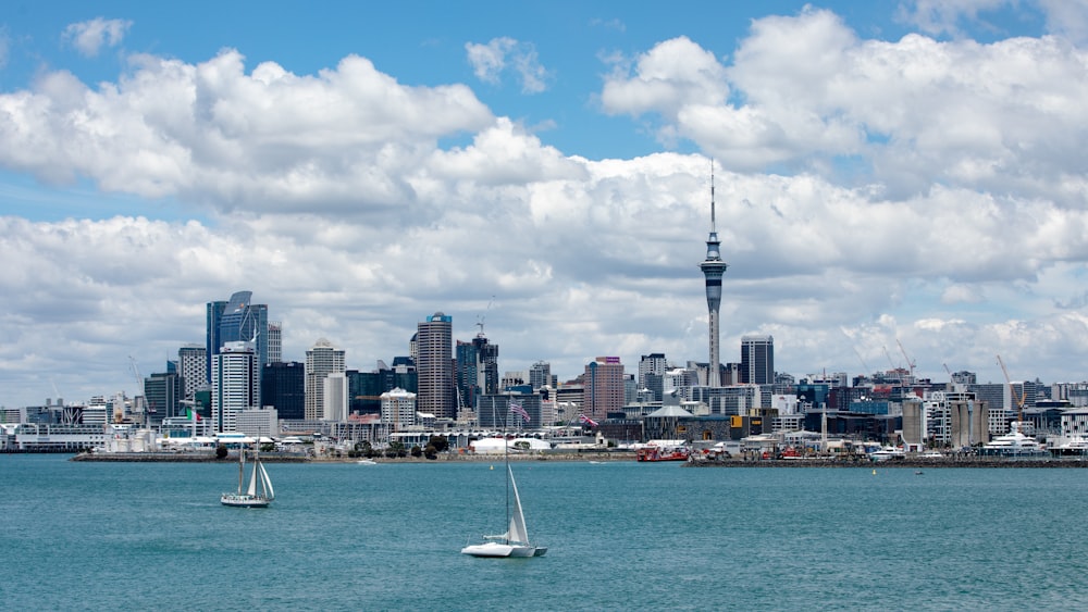 white sailboat on sea near city buildings under white clouds and blue sky during daytime