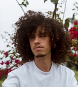 man in white crew neck shirt standing near red flowers