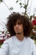 man in white crew neck shirt standing near red flowers