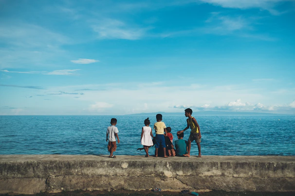 A candid shot of children playing by a rustic wooden pier in a coastal fishing community.