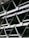 A close-up view of an industrial structure displaying several parallel metallic beams and cross-braces arranged in a geometric pattern. The beams are primarily composed of metal and exhibit a clean, angular design. A light fixture is visible at the top left corner.