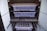 A dark-colored storage cabinet with two transparent plastic containers on separate shelves. Below them, there is a drawer with foam inserts, possibly for organization. The bottom section has metal rods, likely for hanging items, and another plastic container.