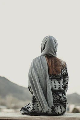 a person sitting on a ledge with a blanket over their head