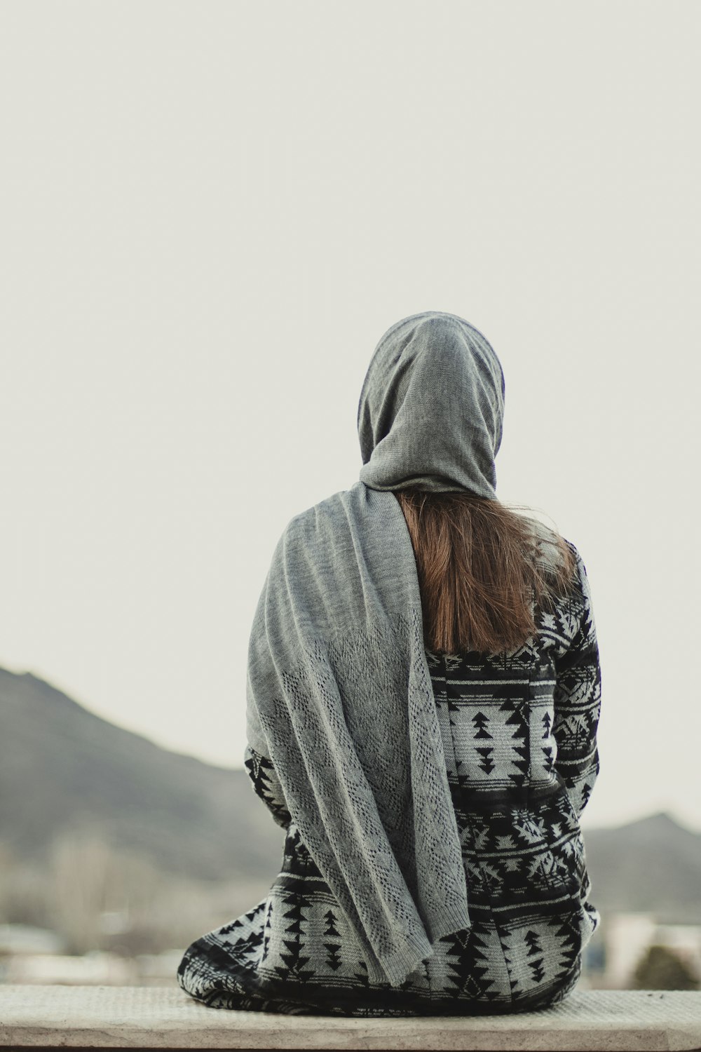 a person sitting on a ledge with a blanket over their head