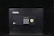 A black electronic safe with a keypad and a small digital display. The safe has a prominent brand logo on the front and a warning label at the top left corner. It is placed in a dark environment, enhancing its prominence and security features.