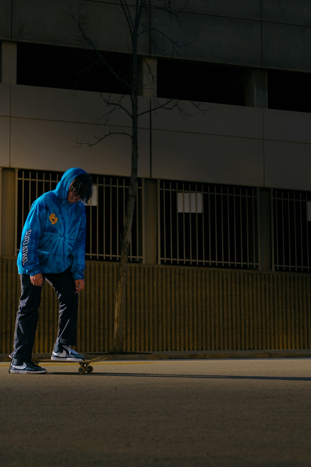 man in blue hoodie and blue denim jeans walking on sidewalk during daytime