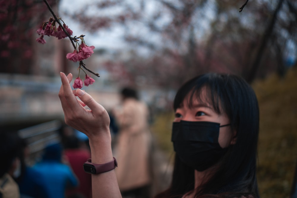 girl in black mask holding pink flower during daytime