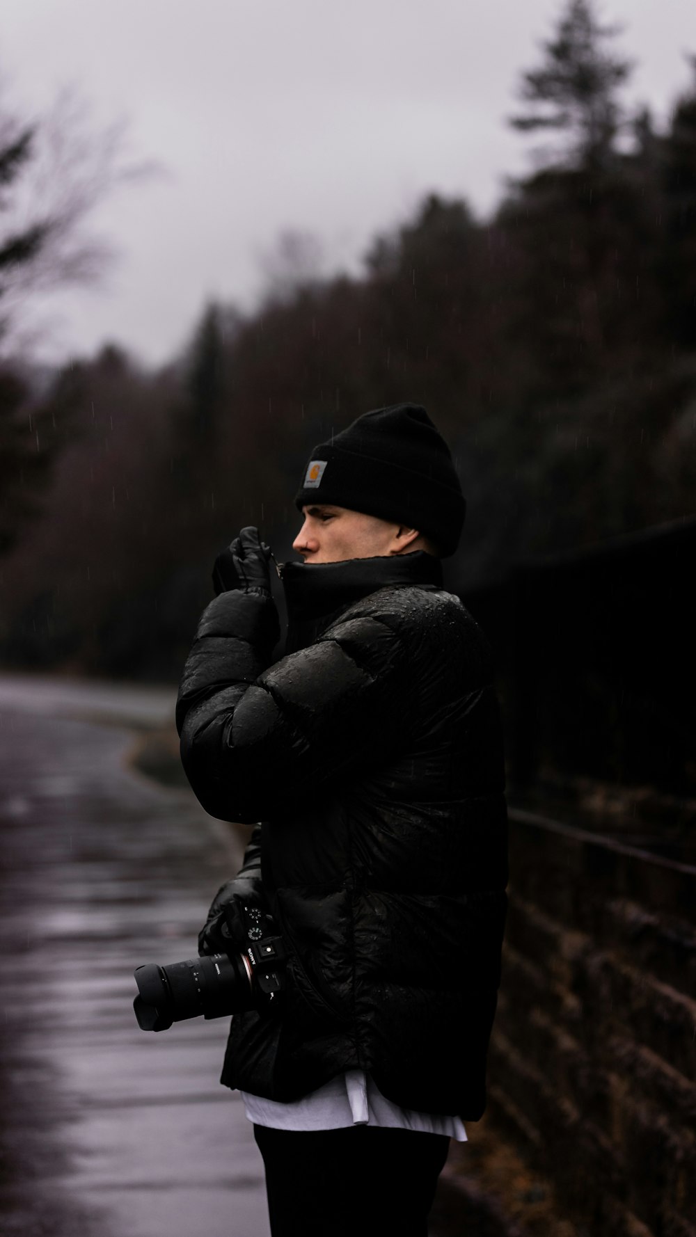 man in black jacket and black knit cap holding black dslr camera