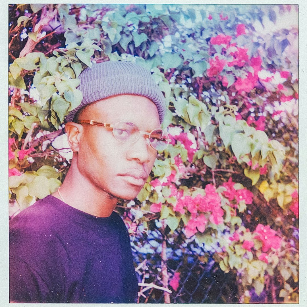 man in black crew neck shirt wearing gray knit cap standing beside red and green leaves