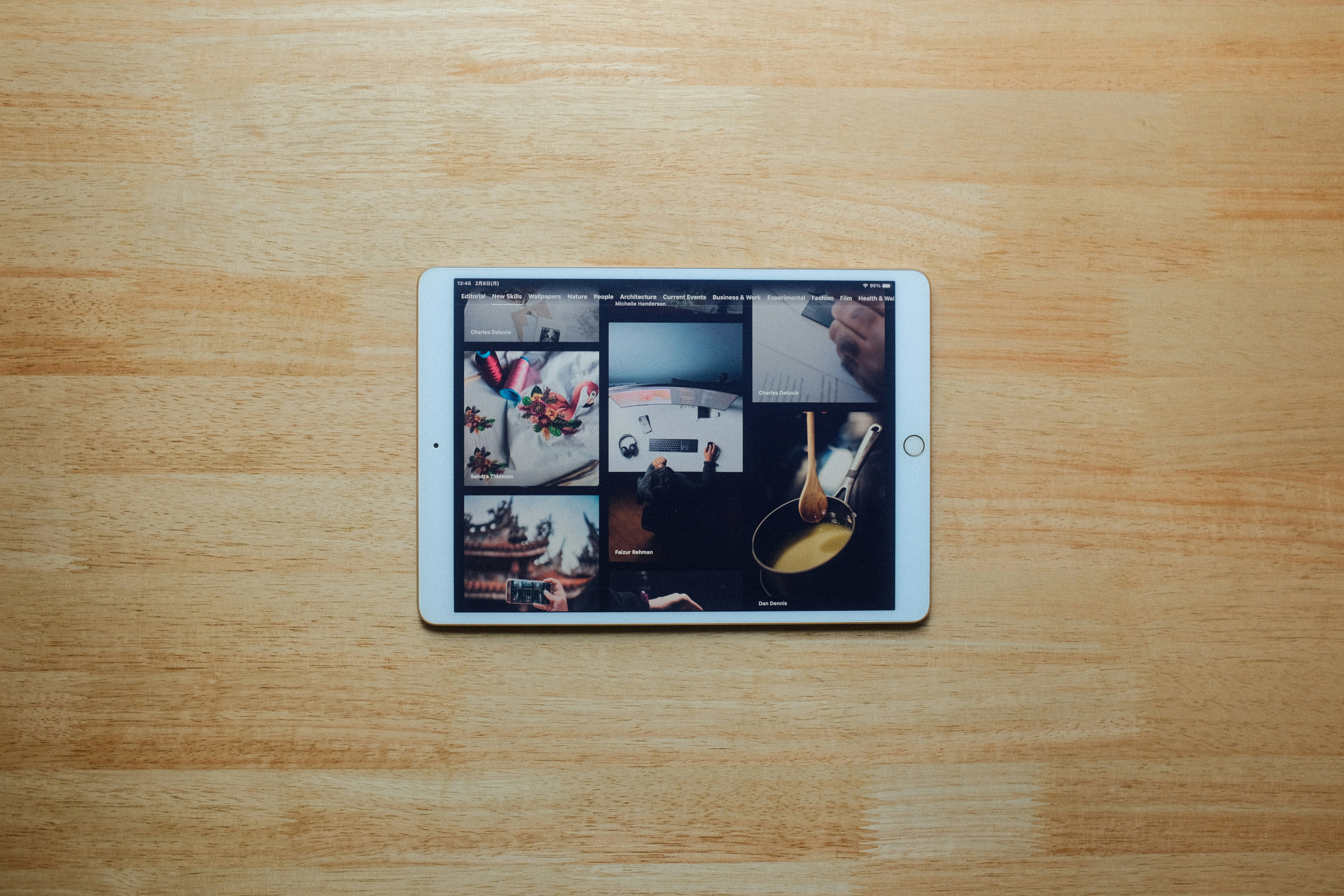 A digital tablet sits on a wooden table displaying image thumbnails.