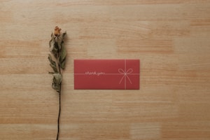 A handwritten thank you note next to a bouquet of fresh flowers and a small gift bag.