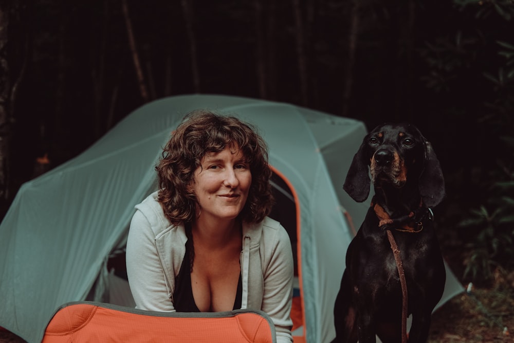 woman in white long sleeve shirt sitting beside black short coated dog