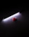 A red light bulb lies on a dark surface beside a strip of bright white LED lights. The LED lights cast a soft glow around them, creating a contrast between the bright light and the darkness of the background.