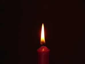 A glowing red candle adorned with a Saint Jude image, flickering softly in a dark room.
