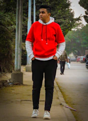 A young man wearing a bold red hoodie and black joggers, mid-run on an urban street.