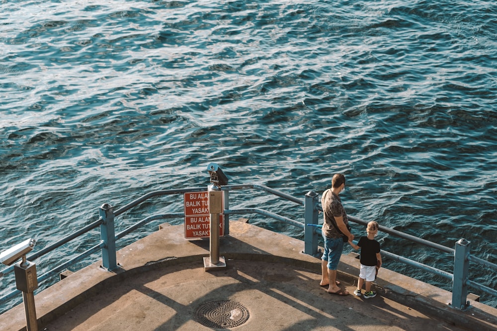 昼間、水域近くのコンクリートの桟橋に立つ男女