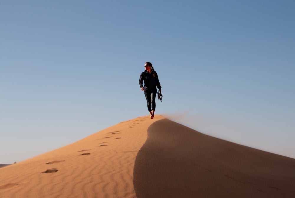 昼間、茶色の砂の上を歩く黒いジャケットの男