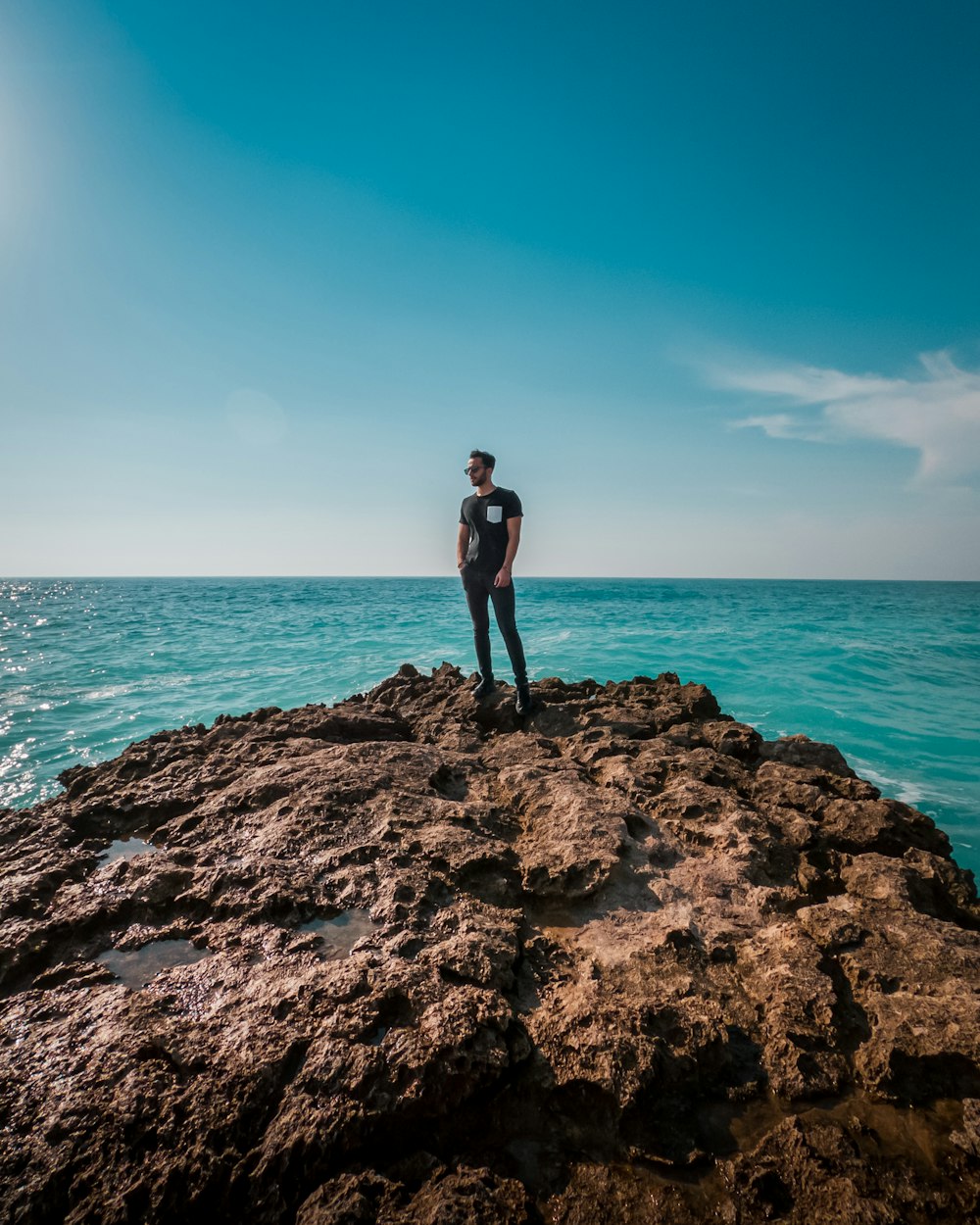 man in black shorts standing on brown rock formation near sea during daytime