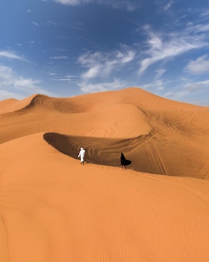 man in black jacket and white pants standing on brown sand under blue sky during daytime