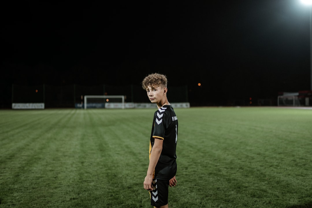 boy in black and white adidas soccer jersey standing on green grass field during nighttime