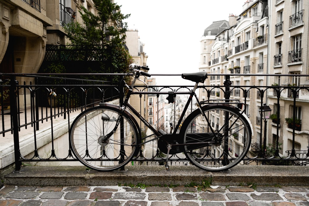 vélo de ville noir garé à côté d’une clôture en métal noir pendant la journée