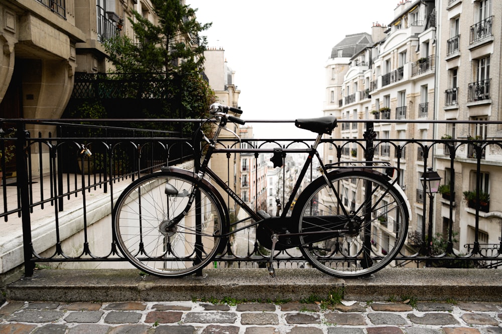 Bicicleta urbana negra estacionada junto a una valla de metal negra durante el día