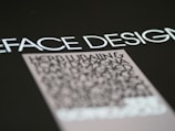 Text in a bold, modern font is prominently displayed against a dark background, with emphasis on the words 'FACE DESIGN'. Below, there is a block of smaller, blurry text that appears to be more detailed but is less legible.