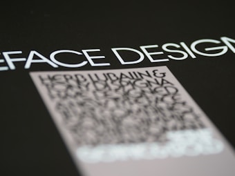 Text in a bold, modern font is prominently displayed against a dark background, with emphasis on the words 'FACE DESIGN'. Below, there is a block of smaller, blurry text that appears to be more detailed but is less legible.