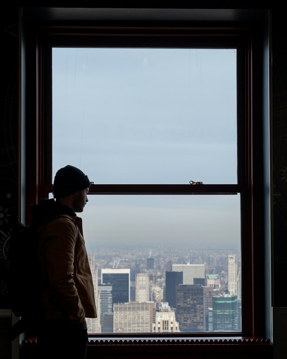 man in brown jacket standing on top of building looking at city during daytime