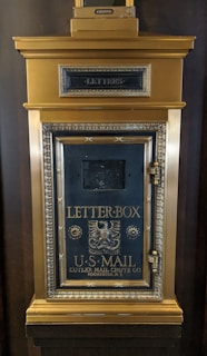 A vintage, ornate, brass and black U.S. Mail letterbox, featuring intricate detailing and the inscription 'Letter Box' and 'Cutler Mail Chute Co., Rochester, N.Y.'. The letterbox has an eagle emblem and is designed with a prominent mail slot and decorative molding.