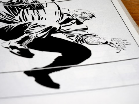 A stylized, high-contrast black and white drawing of a crouching figure with exaggerated features. The illustration appears to be from a comic book, depicting dynamic motion through bold lines and angular shapes. The figure's hand and boot are prominently detailed, capturing a sense of action.
