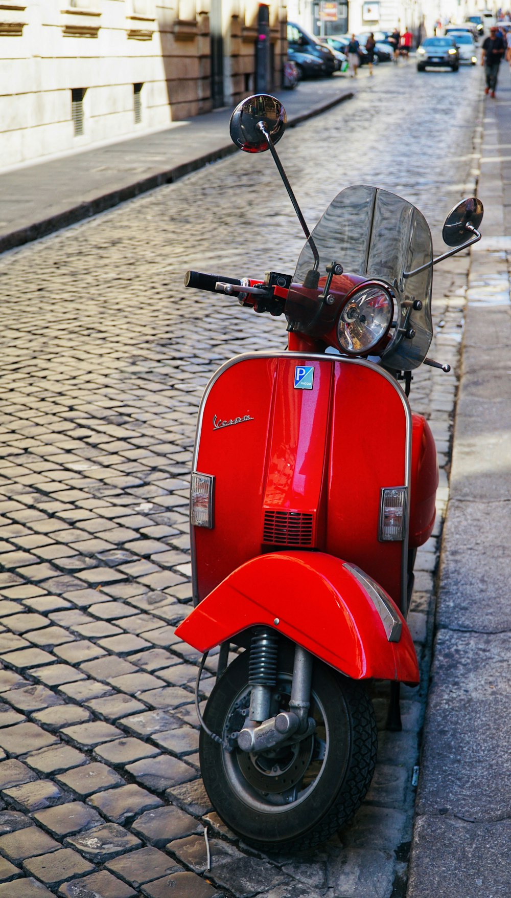 red motor scooter parked on gray brick pavement