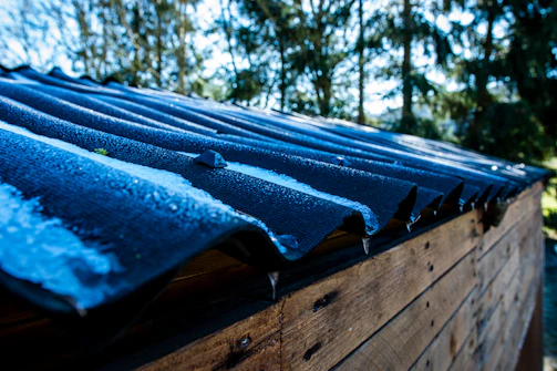 A close-up 4K image showing the steel frame and blue metal roofing of a shed under bright sunlight in India.