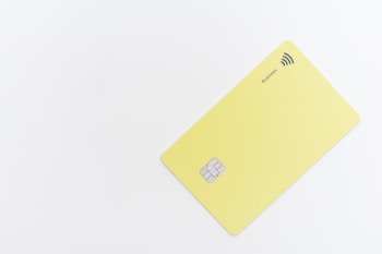 A minimalistic yellow card with a chip and contactless payment symbol is positioned against a white background. The word 'Business' is printed near the contactless symbol.