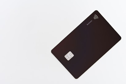 A sleek black card is placed on a white surface, featuring a chip and contactless symbol. The card is oriented diagonally and has a minimalist design with the label 'Business' on the upper right corner.