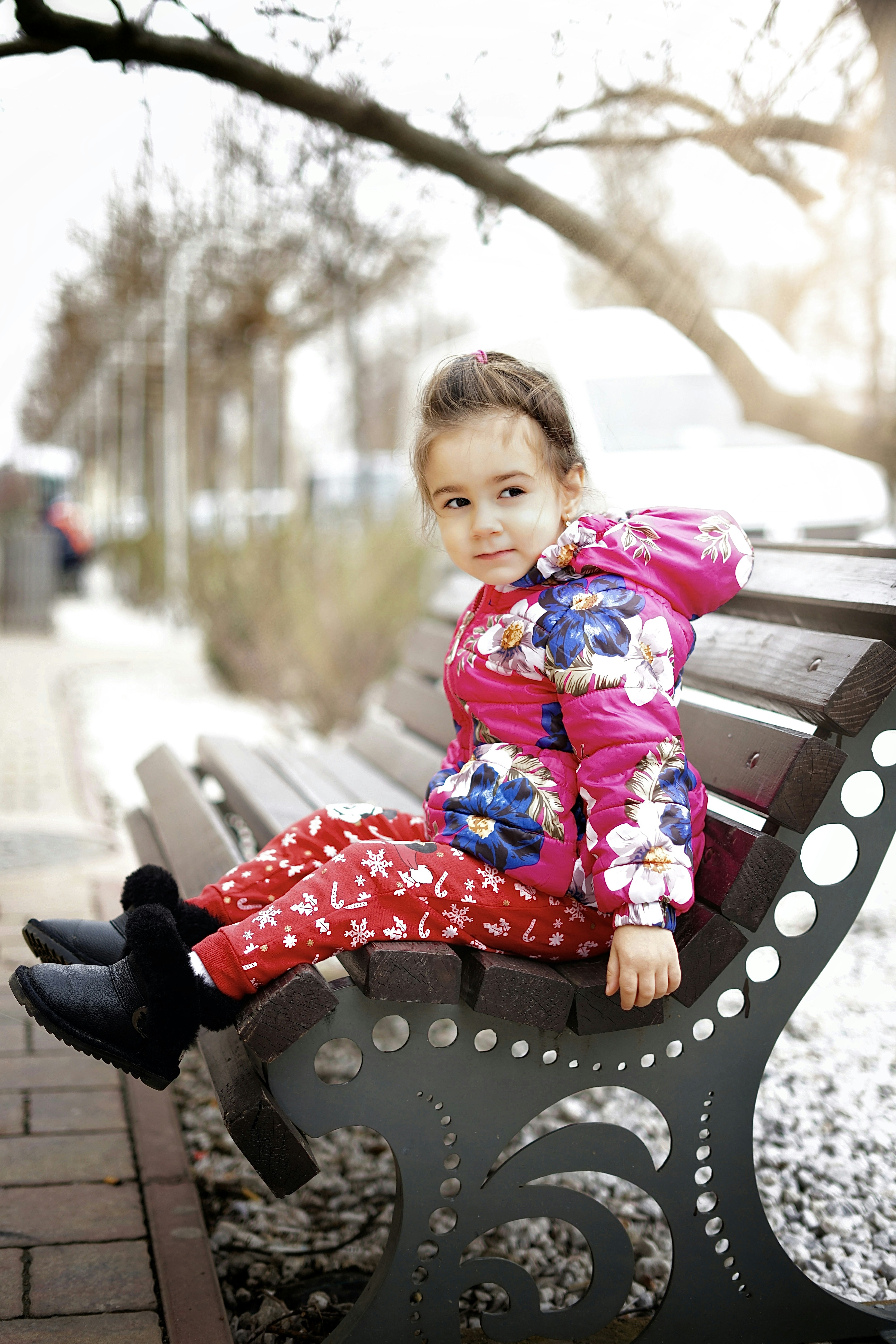 ragazza in abito floreale rosso e bianco che si siede sulla panca di legno marrone durante il giorno