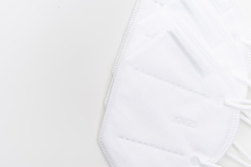 A close-up view of several white KN95 face masks arranged on a light background, showing their texture and layers.